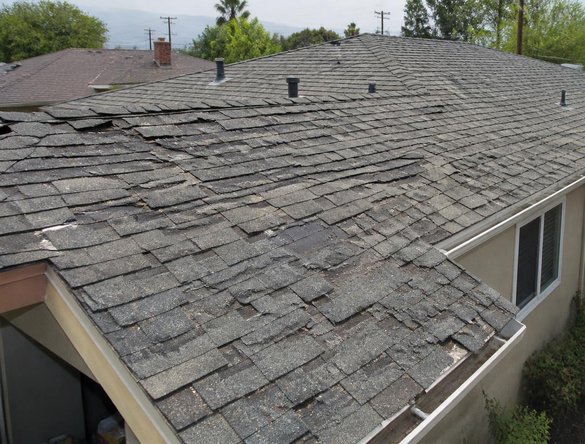 Worn, damaged asphalt shingle roof with curling and missing shingles